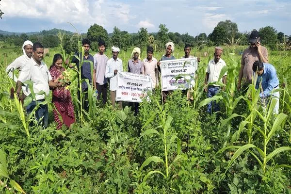 हरे-भरे फसल के खेत में खड़े किसान और कृषि कर्मी, जिनमें दो लोग जानकारी वाले बैनर पकड़े हैं