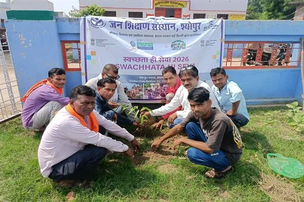 खुले मैदान में एक पौधे के आसपास बैठकर मिट्टी लगाते ग्रामीण और पीछे स्वच्छता ही सेवा का बैनर