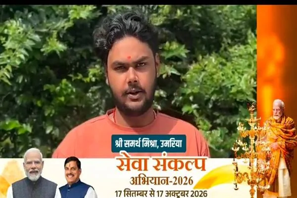 एक युवक हरे पेड़-पौधों के सामने खड़े होकर कैमरे की ओर देखते हुए बात कर रहा है; नीचे की पट्टी पर उनका नाम और एक सरकारी अभियान का बैनर लगा है।